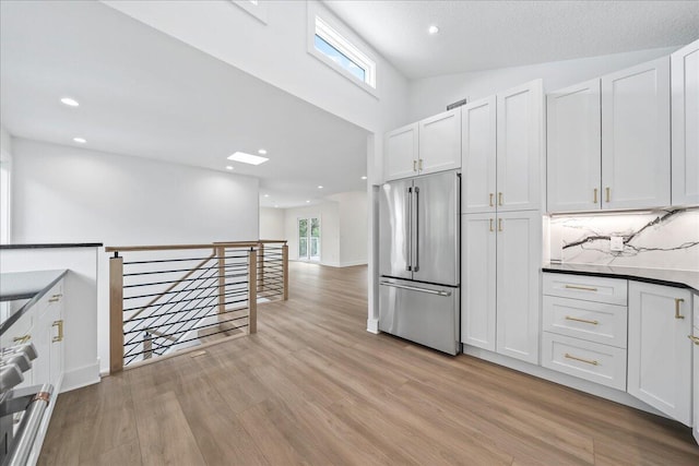 kitchen with a high ceiling, recessed lighting, white cabinets, high end refrigerator, and light wood finished floors