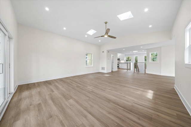 unfurnished living room featuring baseboards, lofted ceiling with skylight, ceiling fan, recessed lighting, and light wood-style flooring