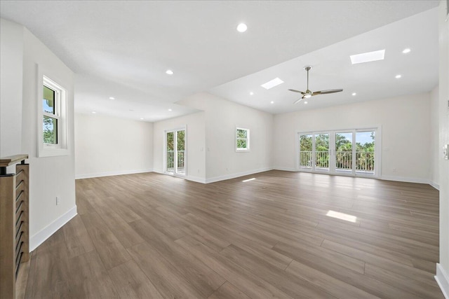 unfurnished living room with a ceiling fan, a skylight, recessed lighting, and wood finished floors