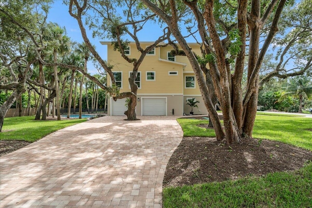 coastal inspired home with a garage, decorative driveway, a front lawn, and fence