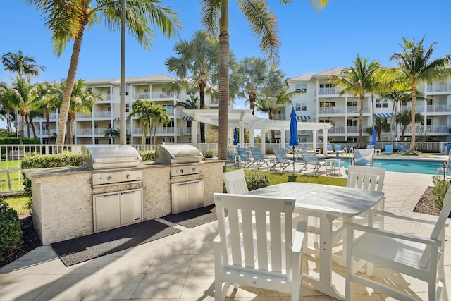 view of patio / terrace with grilling area, a community pool, exterior kitchen, and fence