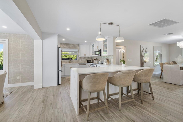 kitchen with light wood-type flooring, stainless steel appliances, kitchen peninsula, and white cabinets