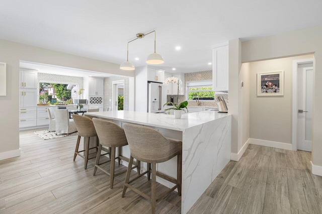 kitchen with white cabinetry, light stone counters, a wealth of natural light, and hanging light fixtures