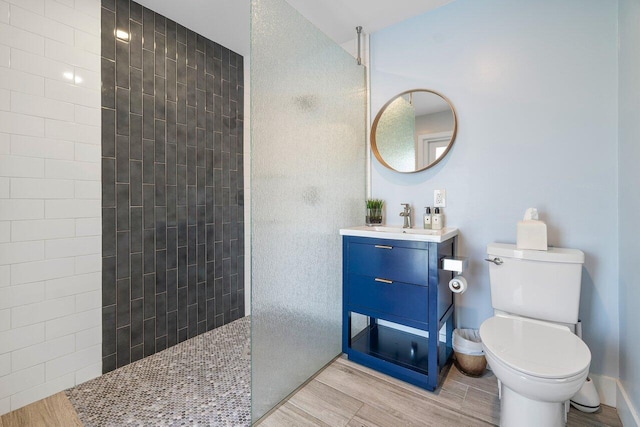 bathroom with toilet, hardwood / wood-style flooring, vanity, and a tile shower