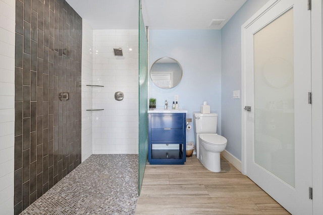 bathroom featuring a tile shower, toilet, vanity, and hardwood / wood-style floors