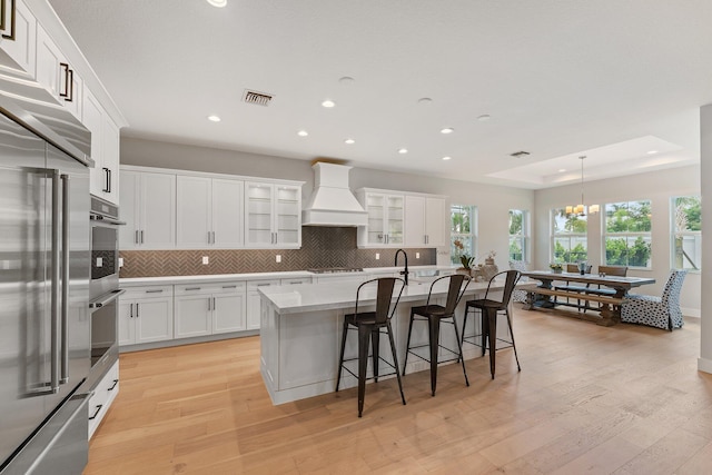 kitchen with light hardwood / wood-style floors, a breakfast bar area, premium range hood, and a kitchen island with sink