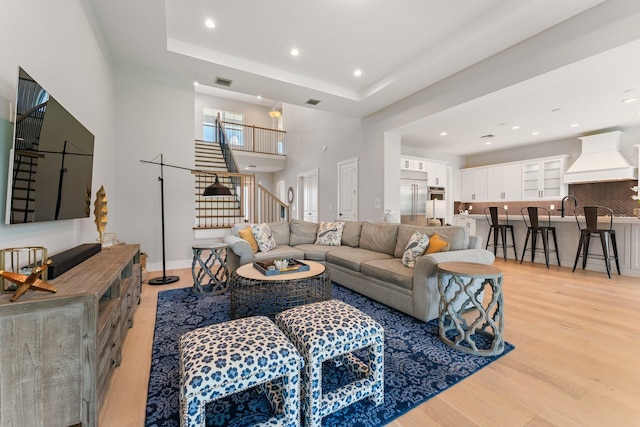 living room featuring sink, a raised ceiling, light hardwood / wood-style flooring, and a high ceiling