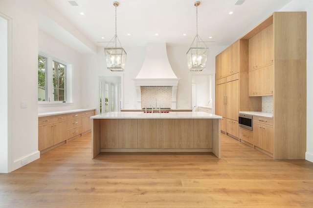 kitchen featuring premium range hood, light brown cabinetry, light hardwood / wood-style floors, decorative backsplash, and a large island with sink