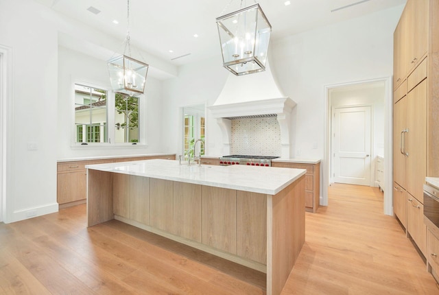 kitchen with light hardwood / wood-style floors, a large island with sink, light brown cabinetry, and decorative light fixtures