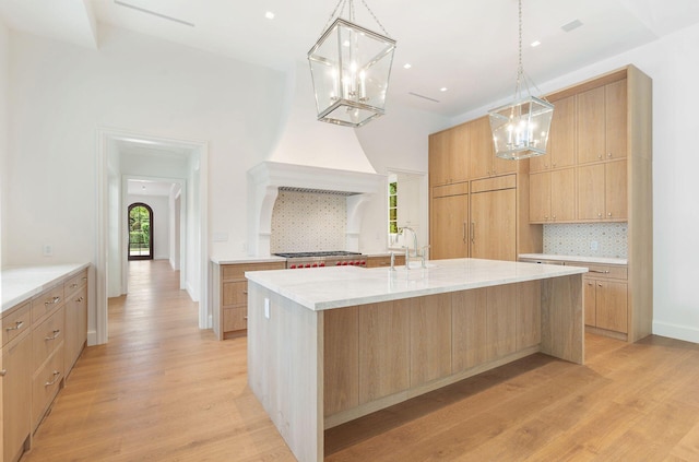 kitchen featuring light hardwood / wood-style flooring, pendant lighting, an island with sink, and backsplash