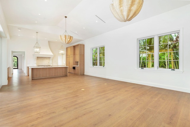 unfurnished living room featuring light hardwood / wood-style floors, an inviting chandelier, lofted ceiling, and sink