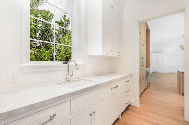 kitchen with sink, white cabinetry, light wood-type flooring, and light stone counters