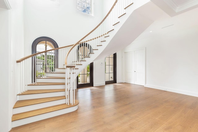 stairs featuring a towering ceiling, hardwood / wood-style flooring, and ornamental molding