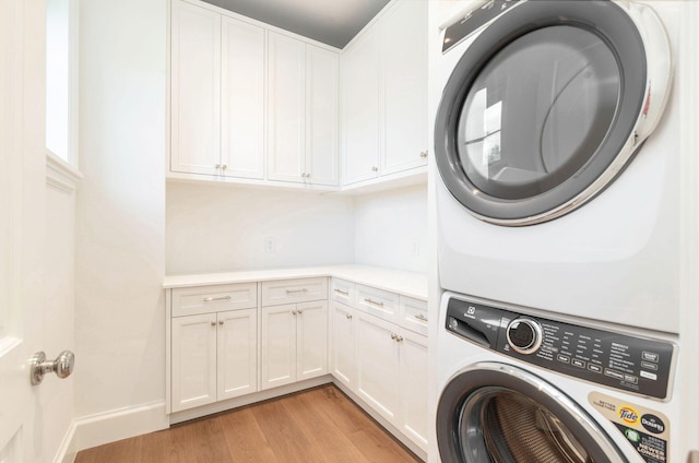 washroom featuring stacked washer and dryer, light wood-type flooring, and cabinets