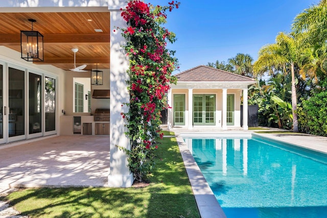 view of swimming pool featuring grilling area, exterior kitchen, ceiling fan, an outdoor structure, and a patio area