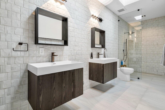 bathroom featuring vanity, tile patterned flooring, toilet, tile walls, and a tile shower