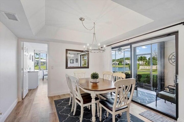 dining space with a tray ceiling, an inviting chandelier, a water view, and hardwood / wood-style flooring