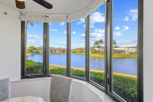 sunroom with ceiling fan and a water view