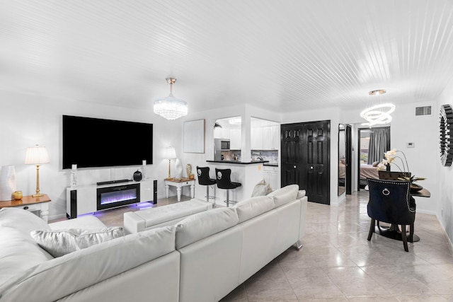 living area featuring visible vents, baseboards, a glass covered fireplace, and a notable chandelier