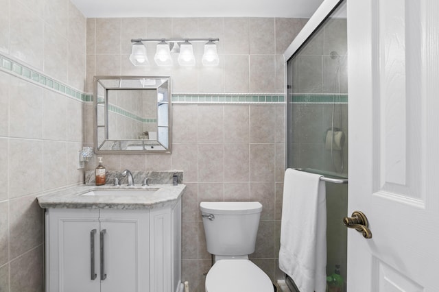 bathroom with vanity, tile walls, toilet, and a shower with door