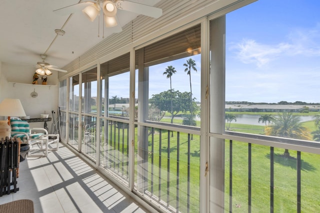 sunroom featuring a water view, tile patterned floors, and a ceiling fan