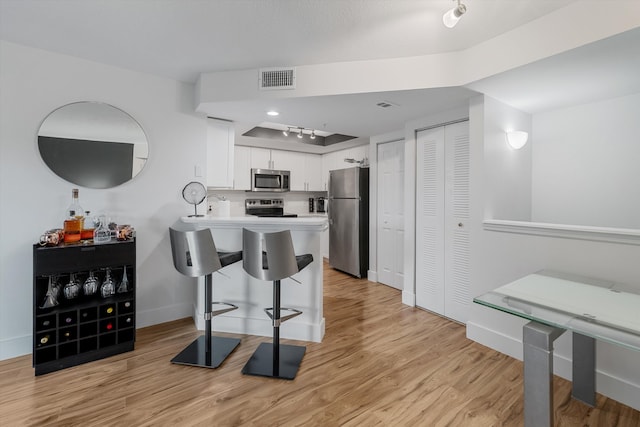 kitchen featuring a breakfast bar, white cabinets, kitchen peninsula, stainless steel appliances, and light hardwood / wood-style flooring