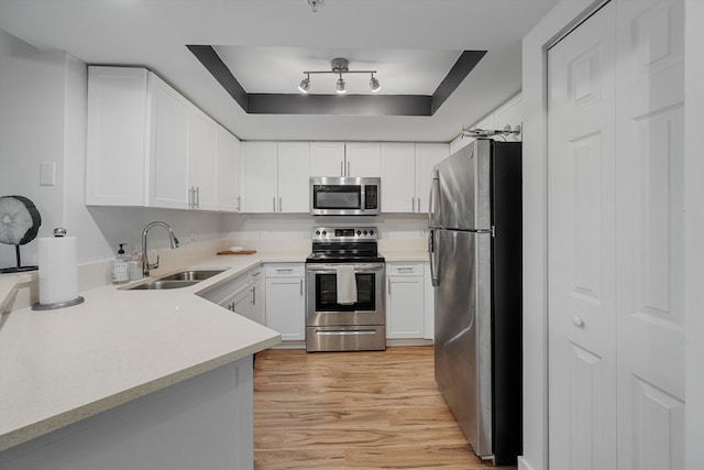 kitchen with light wood-type flooring, sink, white cabinets, stainless steel appliances, and a raised ceiling