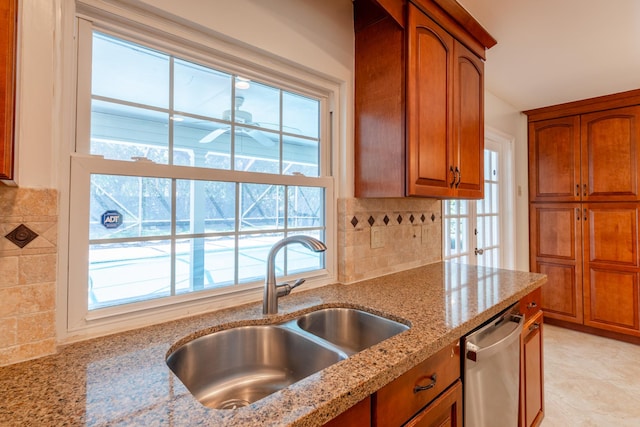 kitchen with light stone countertops, backsplash, sink, and stainless steel dishwasher