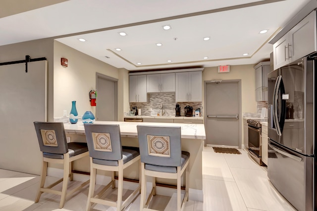 kitchen with stainless steel appliances, a barn door, a kitchen bar, gray cabinets, and light tile patterned floors