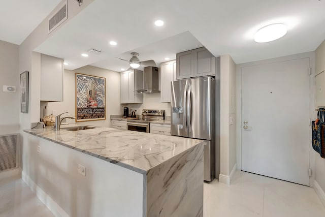 kitchen featuring sink, wall chimney exhaust hood, appliances with stainless steel finishes, light stone counters, and kitchen peninsula