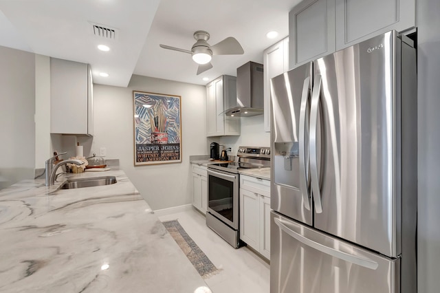 kitchen featuring light stone countertops, sink, ceiling fan, stainless steel appliances, and wall chimney range hood