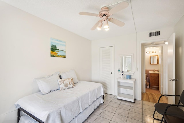 bedroom with ceiling fan, a closet, ensuite bathroom, light tile patterned floors, and a textured ceiling