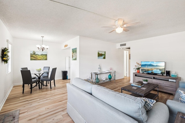 living room featuring ceiling fan with notable chandelier, a textured ceiling, and light hardwood / wood-style flooring