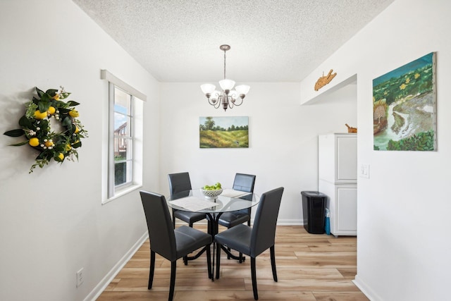 dining area featuring a notable chandelier, light wood-type flooring, and a textured ceiling