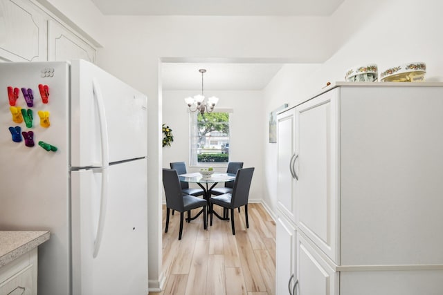 kitchen with light wood-type flooring, white fridge, a notable chandelier, hanging light fixtures, and white cabinetry