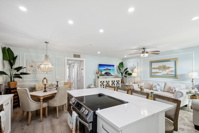 kitchen with stainless steel electric range, hanging light fixtures, light hardwood / wood-style floors, white cabinets, and ceiling fan with notable chandelier