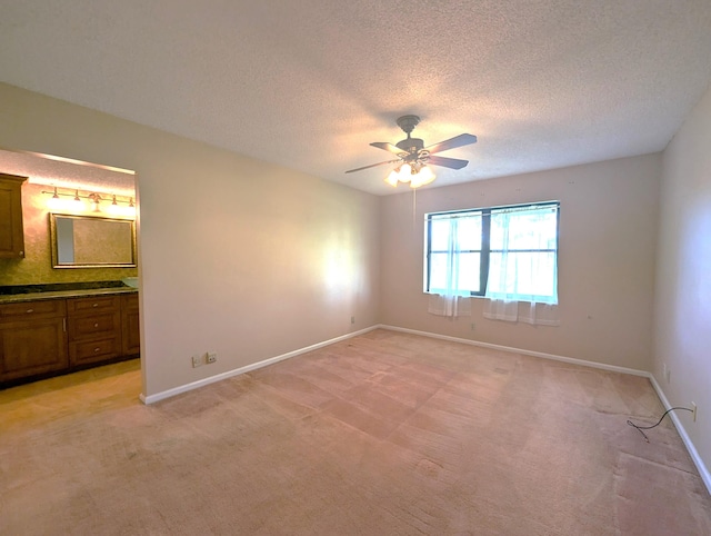 unfurnished bedroom featuring ensuite bath, ceiling fan, light colored carpet, and a textured ceiling