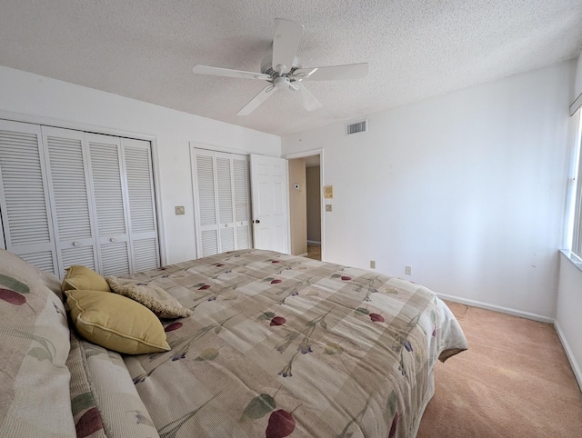 bedroom featuring light carpet, a textured ceiling, two closets, and ceiling fan