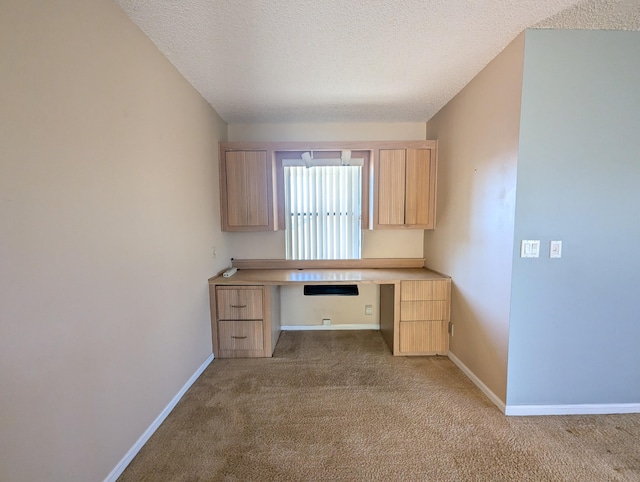 unfurnished office featuring a textured ceiling, built in desk, and light colored carpet