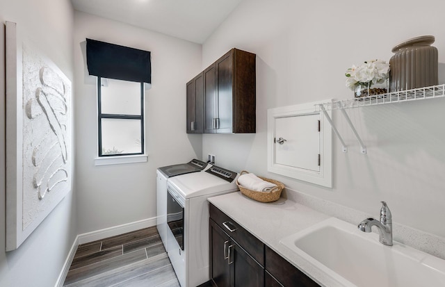 clothes washing area with wood finished floors, baseboards, cabinet space, a sink, and washing machine and dryer