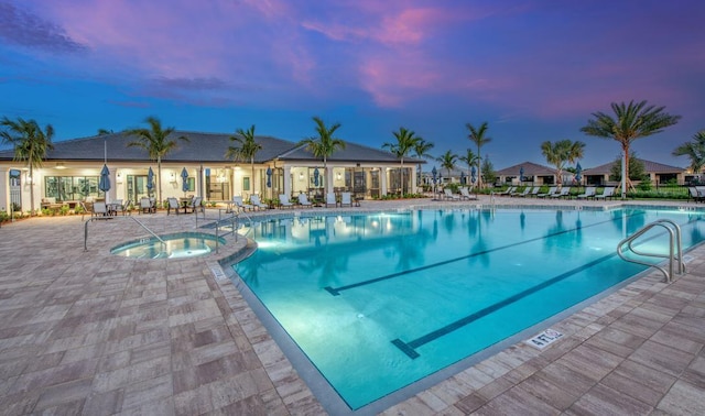 pool at dusk featuring a hot tub, a patio, and a community pool