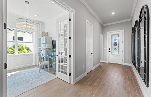 foyer entrance with light wood-style flooring, baseboards, an inviting chandelier, and ornamental molding