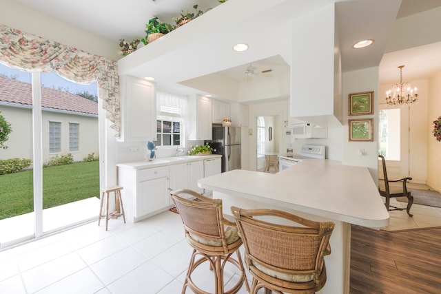 kitchen featuring light hardwood / wood-style floors, kitchen peninsula, a breakfast bar, white cabinets, and white appliances