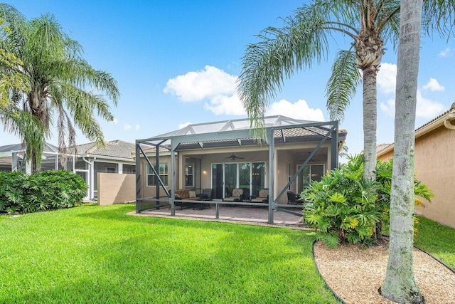 back of property with glass enclosure, ceiling fan, a patio area, and a yard