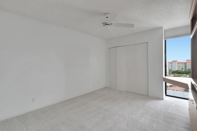 unfurnished bedroom with a closet, light colored carpet, a textured ceiling, and ceiling fan