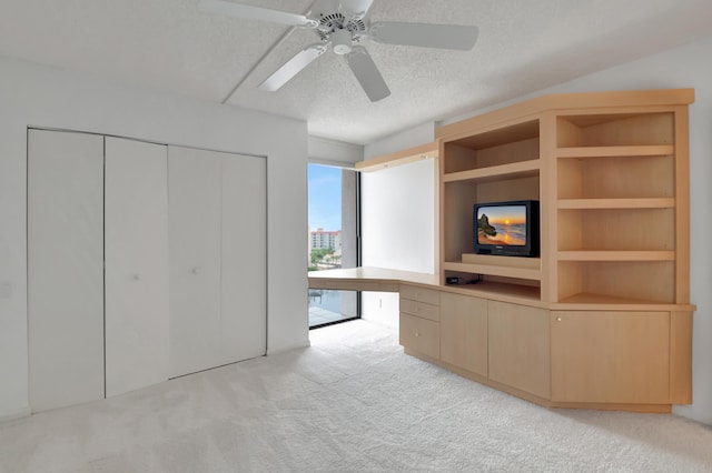 interior space with ceiling fan, light colored carpet, a textured ceiling, and built in desk