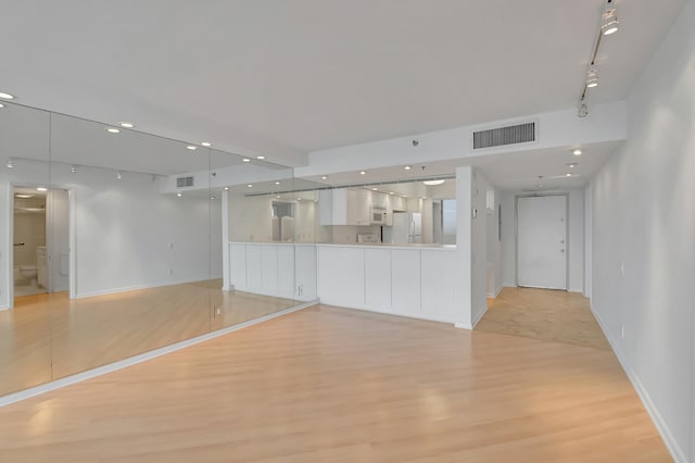 unfurnished living room featuring basketball hoop, light hardwood / wood-style floors, and track lighting