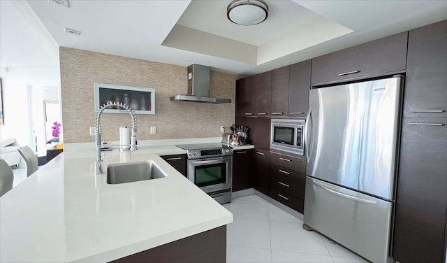 kitchen featuring stainless steel appliances, a raised ceiling, sink, and wall chimney range hood