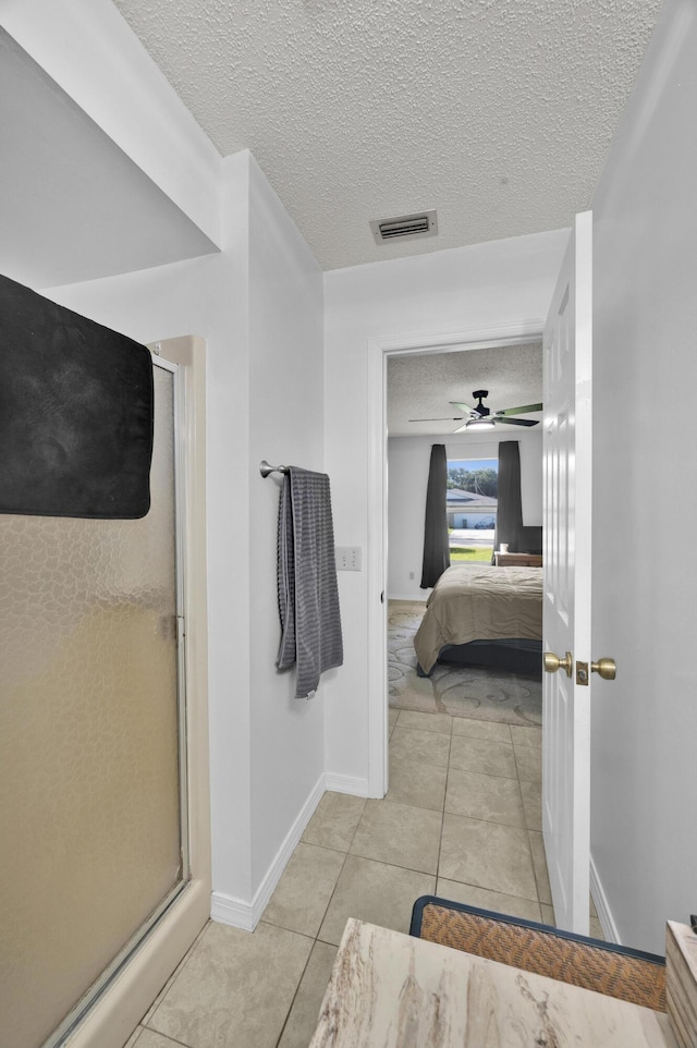 bathroom with a textured ceiling, ceiling fan, a shower with shower door, and tile patterned flooring