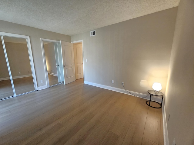 unfurnished bedroom with visible vents, a textured ceiling, baseboards, and wood finished floors